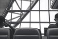 Black and white behind image of a man sitting and waiting for depart while another man talking on a phone