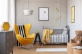 Black and white blanket on yellow egg chair in grey baby bedroom with black wooden stool with mug and grey crib with cozy blanket Royalty Free Stock Photo