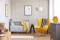 Black and white blanket on yellow egg chair in grey baby bedroom with black wooden stool with mug and grey crib with cozy blanket Royalty Free Stock Photo