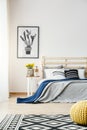 Black and white cactus poster hanging on the wall in bright bedroom interior with yellow fresh flowers, double bed and patterned
