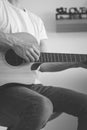 Black and white candid portrait of an artist strumming a guitar at home. He enjoys every chord played. Close-up on a hand playing