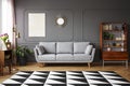 Black and white carpet with geometric pattern placed on the floor in dark living room interior with grey couch, vintage cupboard