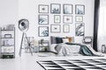 Black and white carpet placed on the floor in bright bedroom interior with king-size bed, black studio lamp and posters hanging on Royalty Free Stock Photo