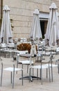 Black and white cat sits beside a glass of water on table of outside resturant deserted in winter with silver tales and white chai