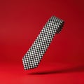 A black and white checkered tie is suspended against a vibrant red background. Royalty Free Stock Photo