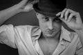 Black and white close portrait of a young man who with his hand adjusts the black hat on his head while looking in front of him Royalty Free Stock Photo