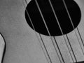 Black and white close-up of ukulele, focus on sound hole top right, strings crossing, shadows below strings Royalty Free Stock Photo