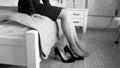 Black and white closeup image of young woman sitting on bed and taking off high heels shoes Royalty Free Stock Photo