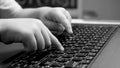 Black and white closeup photo of child pressig buttons on computer keyboard, typing message on laptop keyboard. Royalty Free Stock Photo