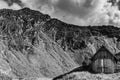 Black and white composition of barn in a mountain scenery with mountain in the background and puffy clouds above Royalty Free Stock Photo