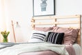 Black and white cushions placed on double bed with wooden bedhead in bright room interior with poster, fresh flowers and lamp