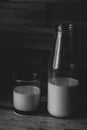 Black and white photo of half a bottle of fresh milk and poured in a glass a wooden background Royalty Free Stock Photo