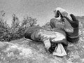 Black and white dashed retro sketch. Hiker high boots and sweaty grey socks. Resting on the boulder at stream