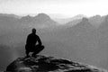 Black and white dashed retro sketch. Moment of loneliness. Man sit on the peak of rock and watching into mist and fog in valley. Royalty Free Stock Photo