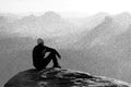 Black and white dashed retro sketch. Moment of loneliness. Man sit on the peak of rock and watching into mist and fog in valley. Royalty Free Stock Photo