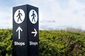 Black and white freestanding directional sign post with arrows and person symbol icon pointing towards shops. Royalty Free Stock Photo