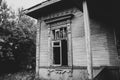 A black-and-white image of an abandoned wooden village house with broken windows near trees Royalty Free Stock Photo