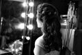 Black and white image of archer woman from back in white dress with bow and arrow on studio lights on background.