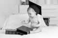 Black and white photo of baby boy in graduation cap sitting on bed and looking on big pile of books Royalty Free Stock Photo