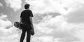 Standing boy posing with his back turned while looking at the sky holding his skateboard and cap Royalty Free Stock Photo