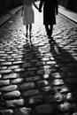 Black and white image of bride and groom holding hands and walking on a cobblestone street, capturing a moment of Royalty Free Stock Photo