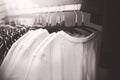 A black-white image of casual t-shirts hanging on hangers in the wardrobe. Shopping in a clothing store. Stylish things