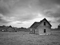 Black and white image of dreary abandoned dilapidated farm house and barn in northern Minnesota