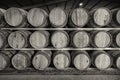 A black and white image of a front on view of a row of stacks of traditional full whisky barrels, set down to mature, in a large