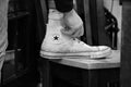 Black and white image of hand tying well worn Converse sneaker