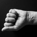 Black & white image of man`s clenched fist and wrist, isolated against a black background with dramatic sidelight