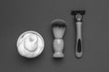 A black and white image of a razor, shaving foam and a shaving brush
