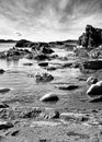 Black and white image showcases the jagged dark ocean rocks beneath a dramatic sky on a bright day