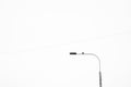 A black and white minimalistic shot of a street lamp and a bird is sitting on it. A thin wire is against the white sky Royalty Free Stock Photo