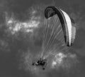 Black and white monochrome illustration of a flying motorized paraplane with people on a background of clouds.