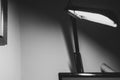 Black and white monochrome image of articulated desk lamp with black arms in foreground blur and with light bulb illuminated with
