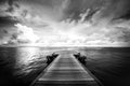 Dramatic jetty pier with white clouds over dark sea bay. Black and white travel landscape background Royalty Free Stock Photo