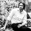 Black-white outdoor portrait of elegant long hair handsome man siting near pond Royalty Free Stock Photo