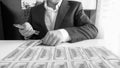 Black and white image of businessman sitting behind desk and laying money in rows Royalty Free Stock Photo