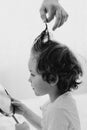 Black and white photo. Father cuts her son hair in the room. Family during quarantine, Scissors and a comb in male hands