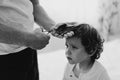 Black and white photo. Father cuts her son hair in the room. Family during quarantine, Scissors and a comb in male hands