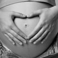 Black and white photo of female on 6th month of pregnancy. Woman touching with hands her naked belly and shows heart sign