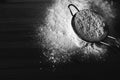 Black and white photo of flour scattered in strainer on a wooden board