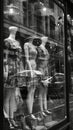 Black and white photo of glass storefronts with manikins, manikins in sold clothes