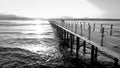 Black and white image of long wooden pier in the ocean. Calm sea waves and amazing sunset over the mountains Royalty Free Stock Photo