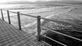 Black and white image of long wooden pier in the ocean. Calm sea waves and amazing sunset over the mountains Royalty Free Stock Photo