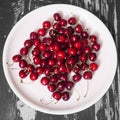 Black and white photo of a lot of fresh sweet cherry fruit berries with water drops. Close-up on the plate on wooden background. Royalty Free Stock Photo