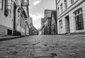 Black and white photo from a low angle shot to a historical cobblestone alley with colorful half-timbered houses