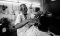 A black and white photo of a male barber giving a haircut in a shop in Phuket, Thailand