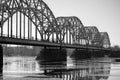 Black and white photo of a metal arched bridge over a river with bridge piers in the water Royalty Free Stock Photo
