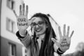 Black and white photo of modern girl with long dreadlocks and eyeglasses in nude color trench showing hands with slogan Royalty Free Stock Photo